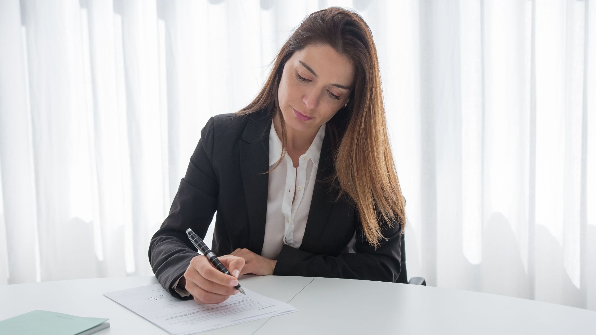 A professional woman in a suit signing paperwork at a desk, showcasing corporate elegance.