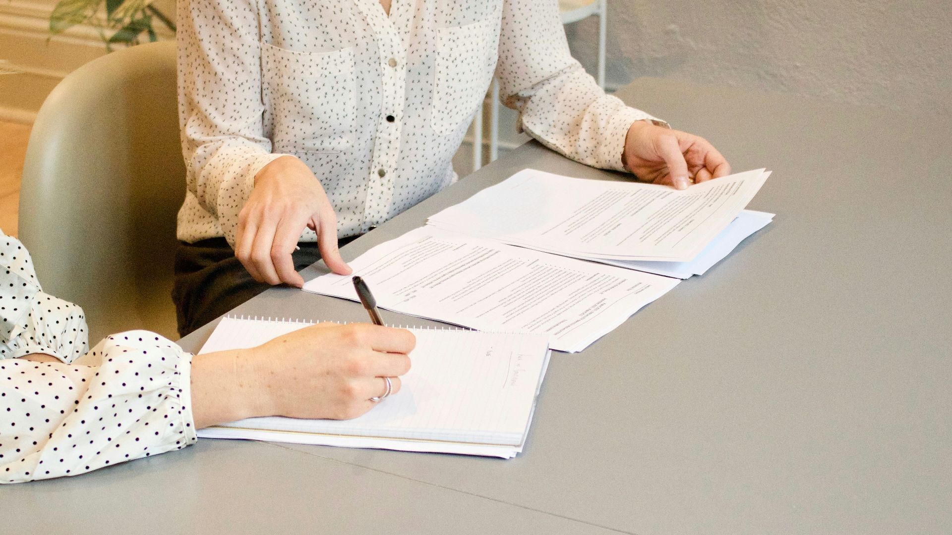 woman signing on white printer paper beside woman about to touch the documents