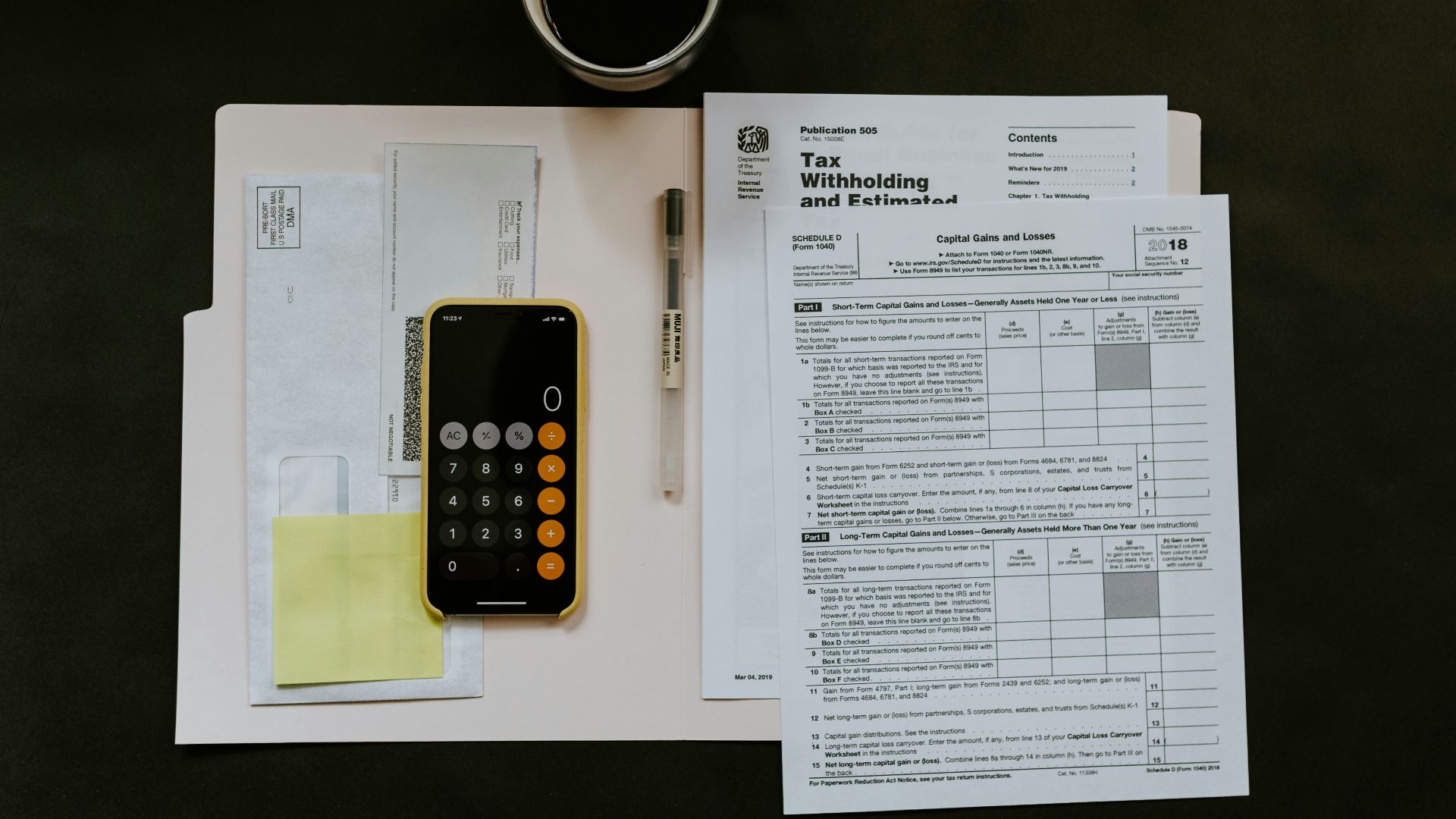 black Android smartphone near ballpoint pen, tax withholding certificate on top of white folder