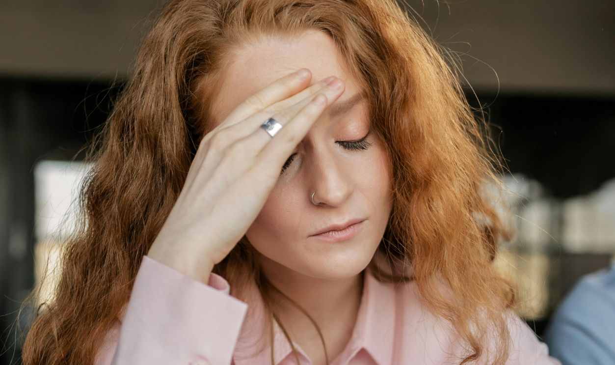 Stressed woman with red hair in pink shirt facing work pressure. Indoor office scene