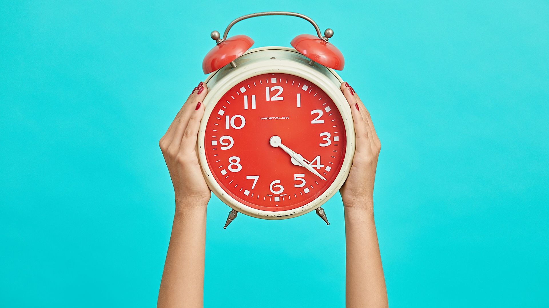 person holding red and beige twin bell analog alarm clock