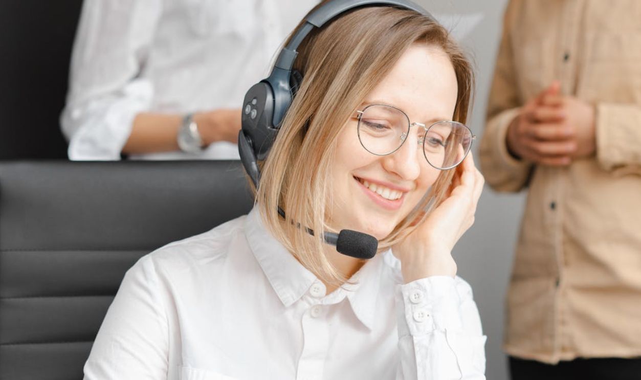 A cheerful woman working at a call center, wearing a headset and glasses, providing excellent customer support
