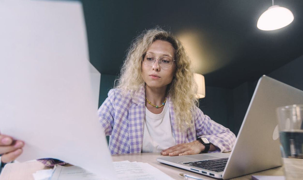 Woman in an office environment reviewing documents with focus, surrounded by technology