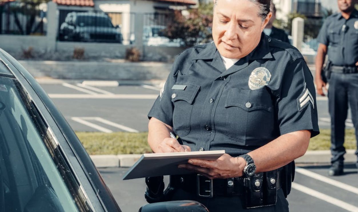 Police officer writing a ticket to a car in a sunny parking lot with a colleague in the background