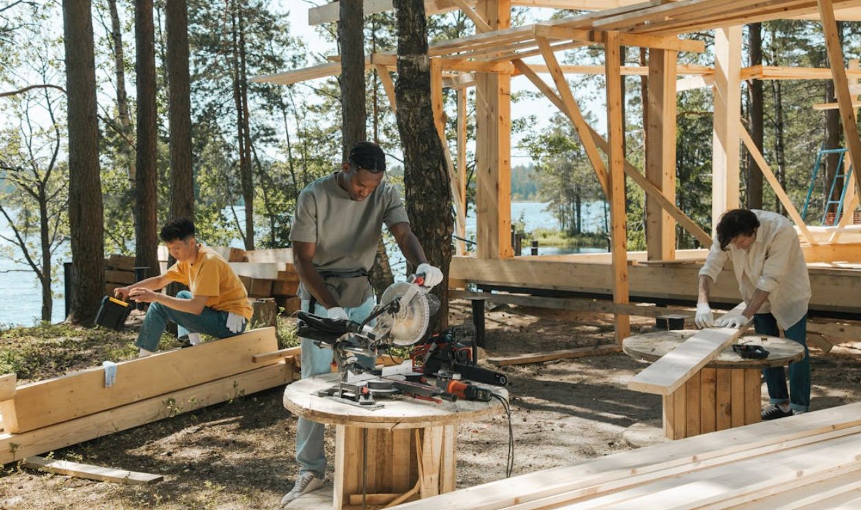 Team of diverse workers engaged in carpentry at a forested lakeside construction site