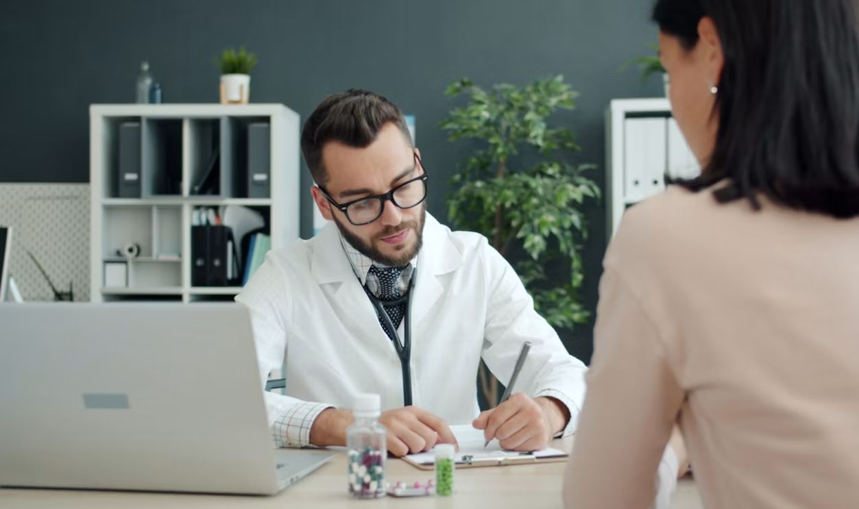 Doctor writing notes while patient sits opposite