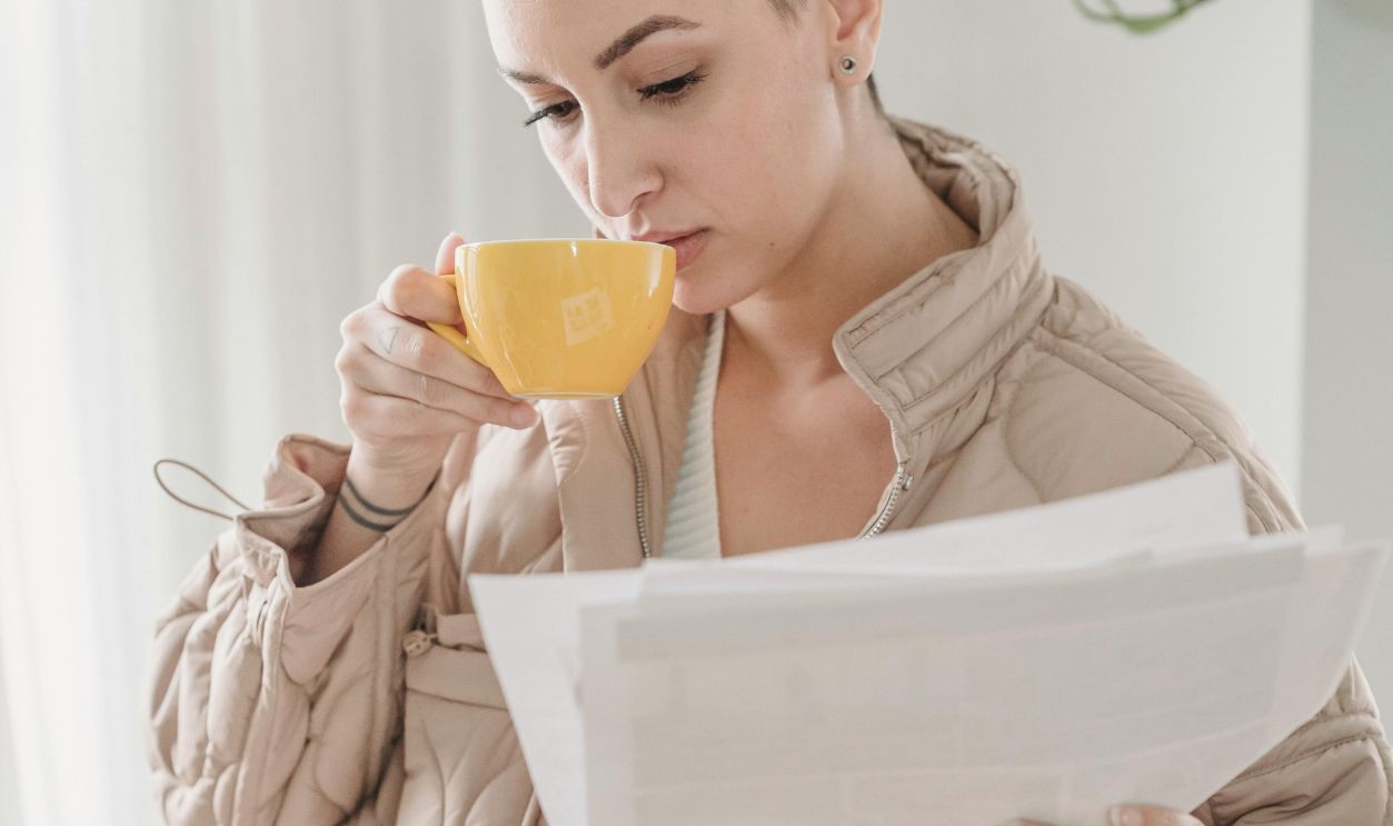 Young woman drinking coffee and reading documents in a cozy indoor setting.