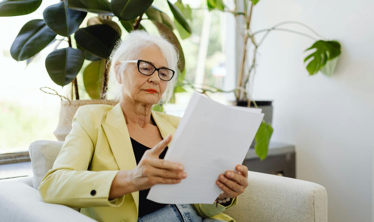 Elderly woman in yellow blazer reading papers