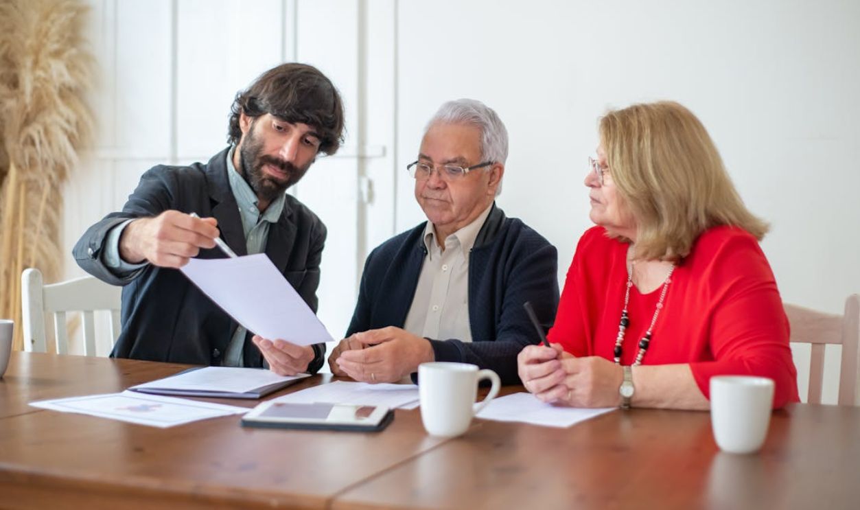 Elderly couple discussing documents with advisor at a wooden table indoors