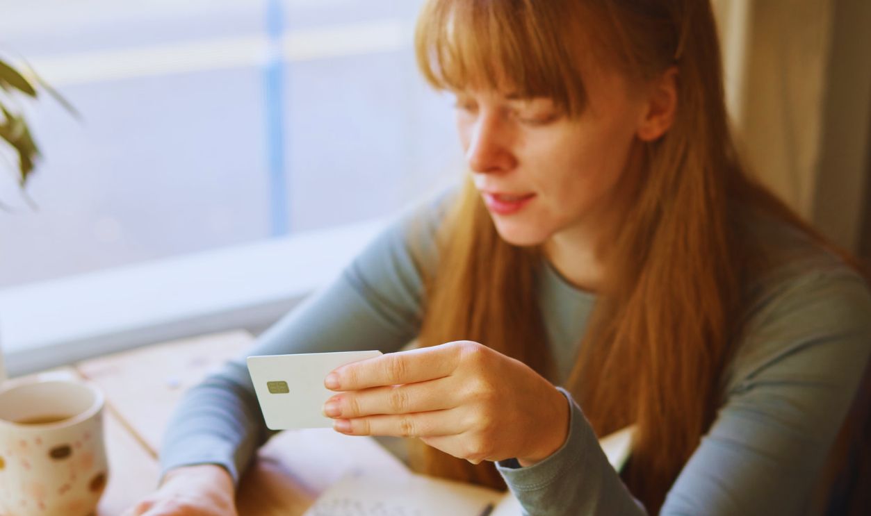 Woman using a laptop for online shopping with a credit card, sitting by a window