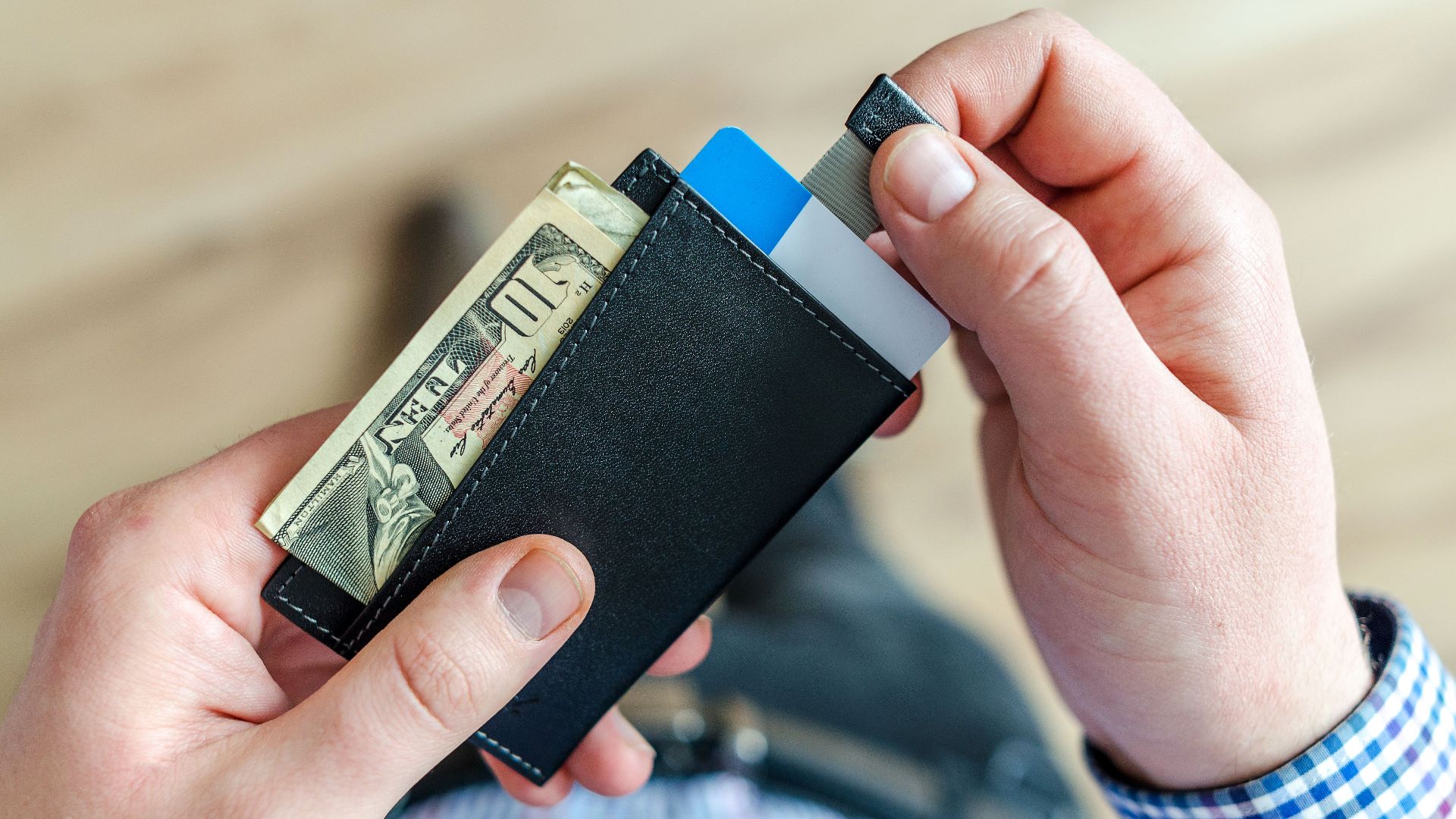 Close-up of a man's hands holding a wallet with cash and credit cards, indicating financial management.