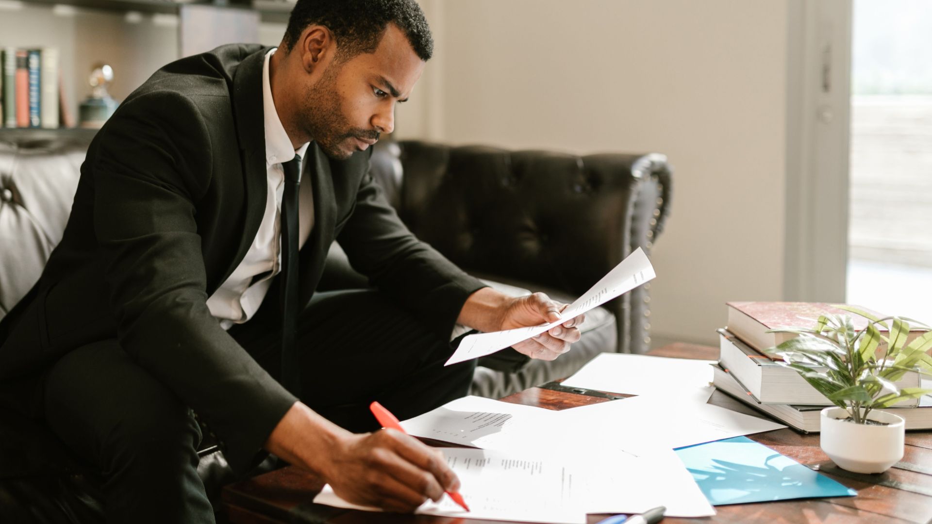 Man in suit signs papers at a coffee table indoors, symbolizing professionalism.