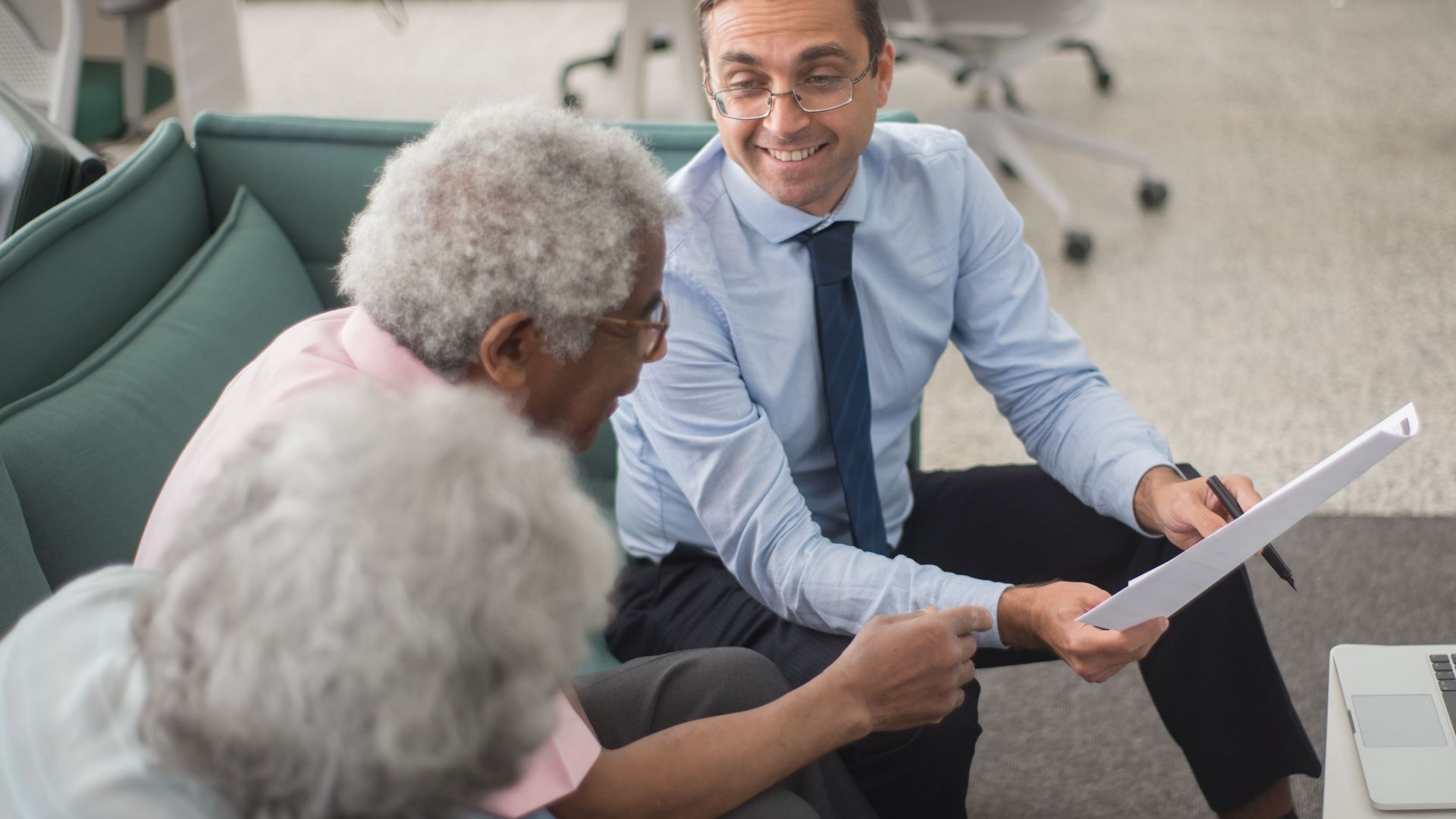 Consultant discussing financial plans with senior clients in a modern office setting, using documents and a laptop.