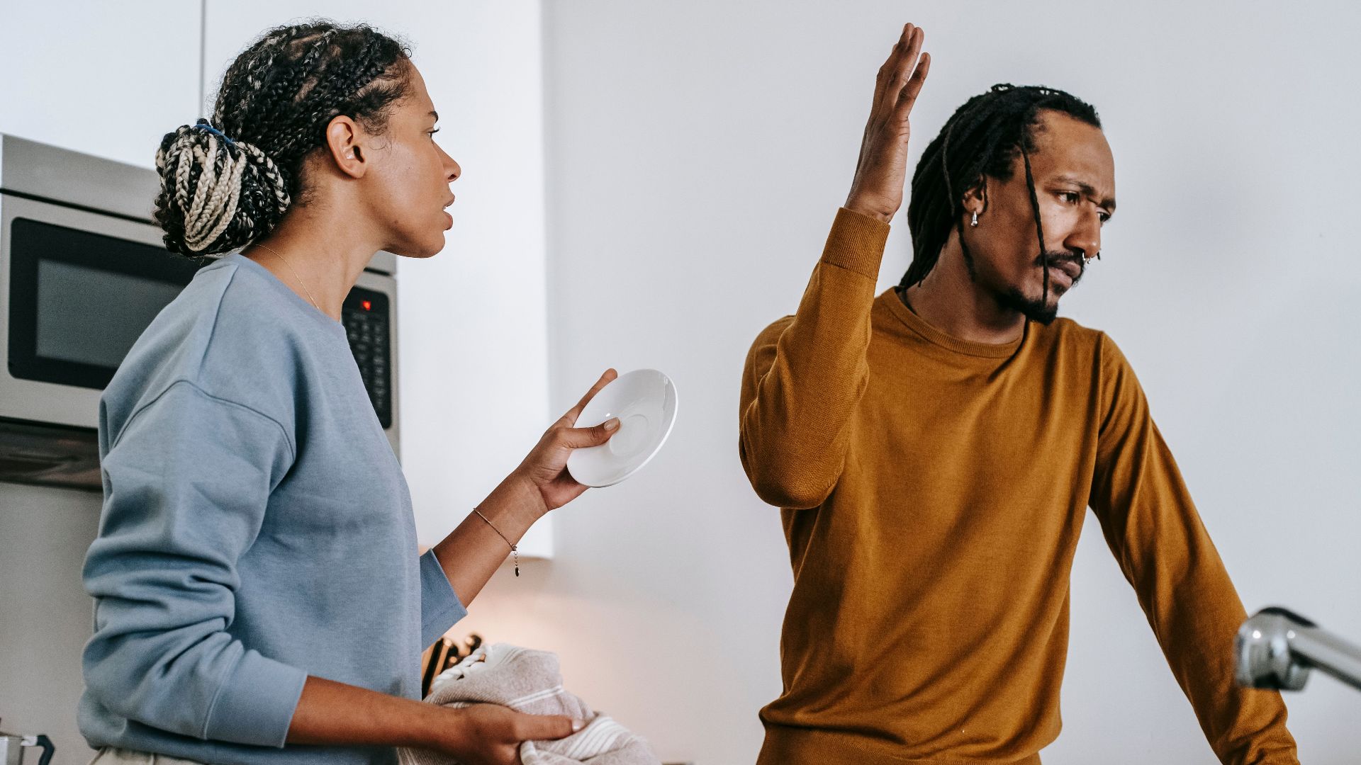 Young dissatisfied African American man with raised arm having conflict with girlfriend in house