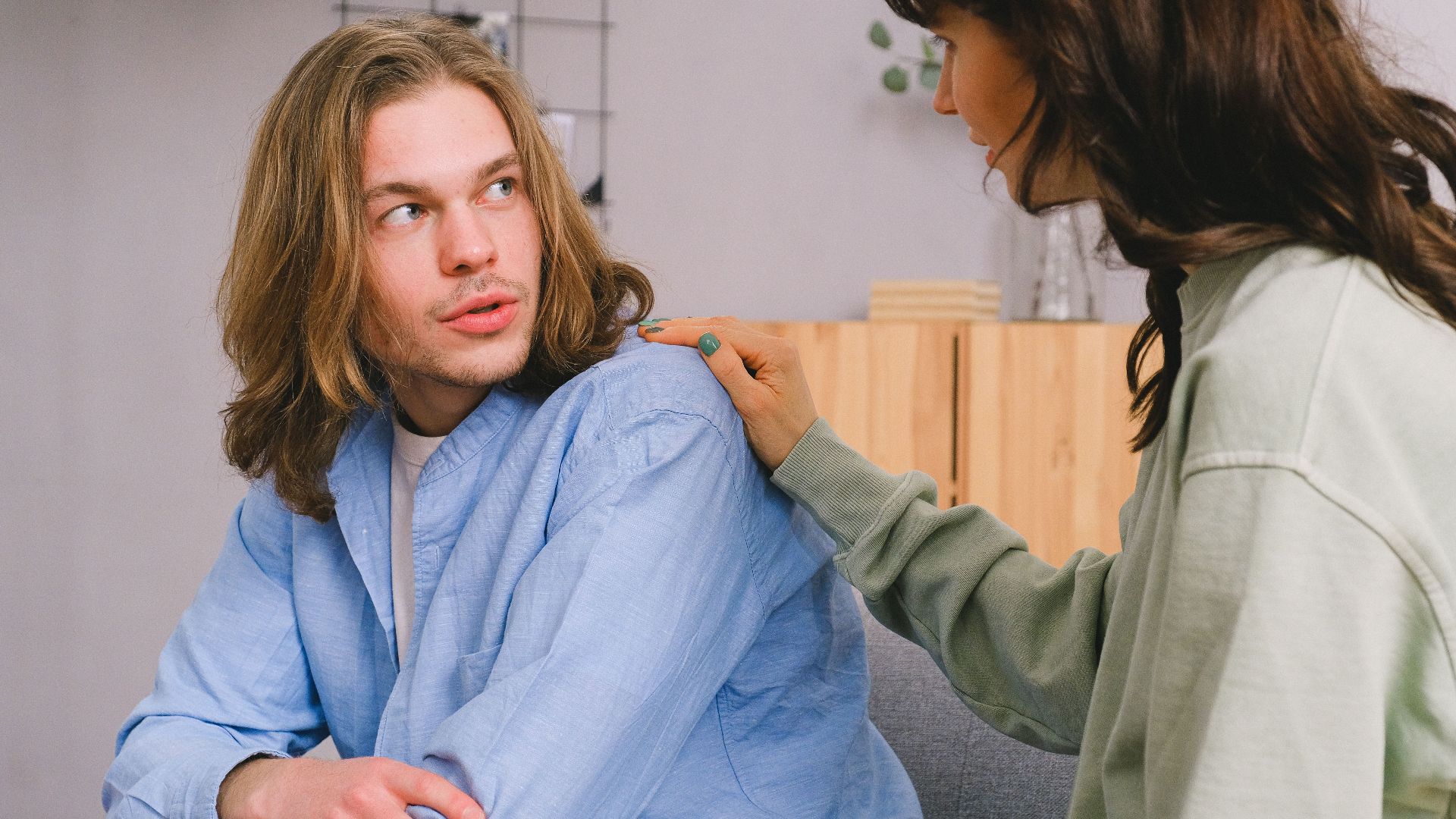Concentrated woman talking and touching shoulder of pensive male in light room in daytime