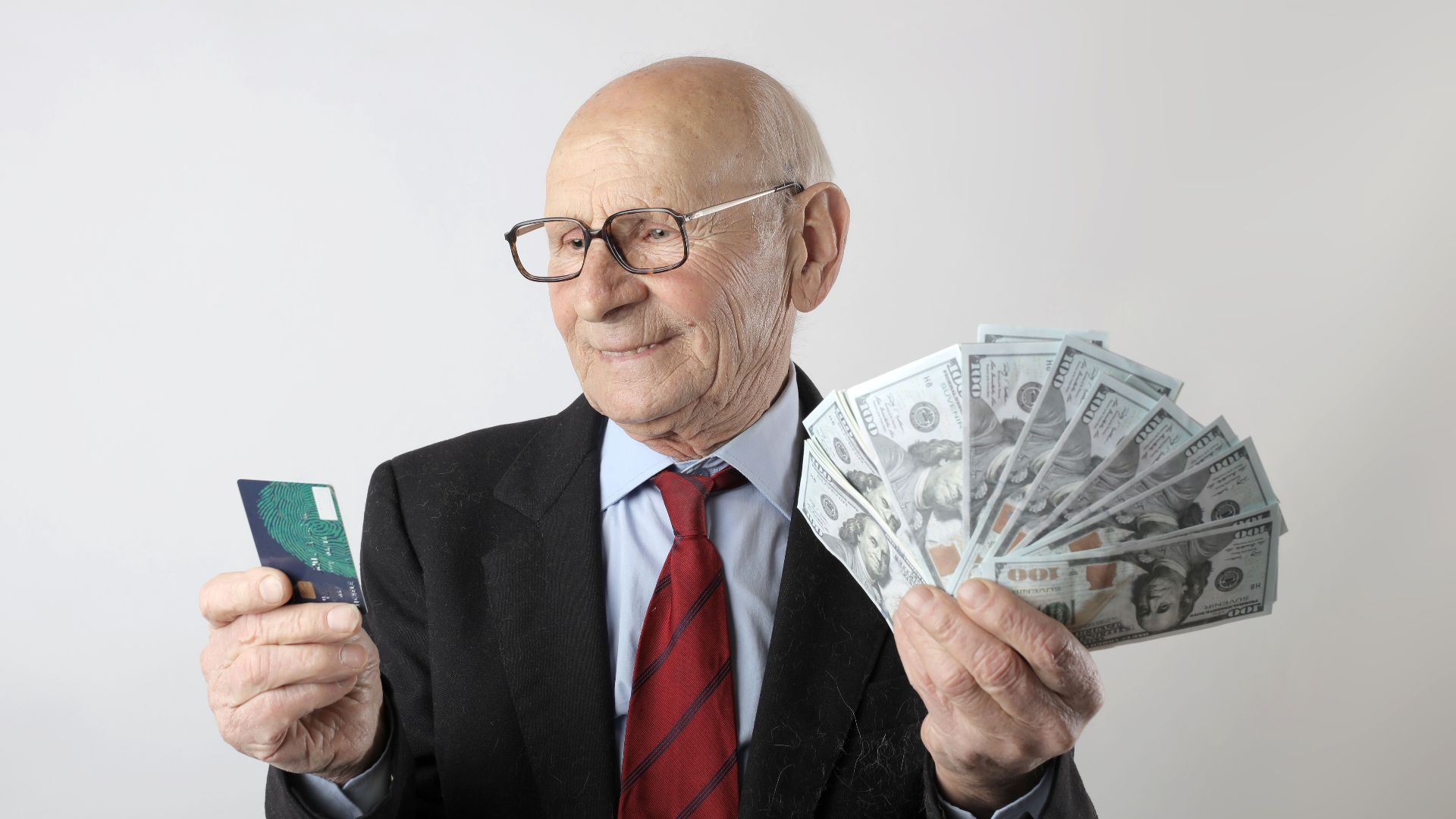 Elderly man in a suit holding a credit card and US dollar bills, representing finance and wealth.