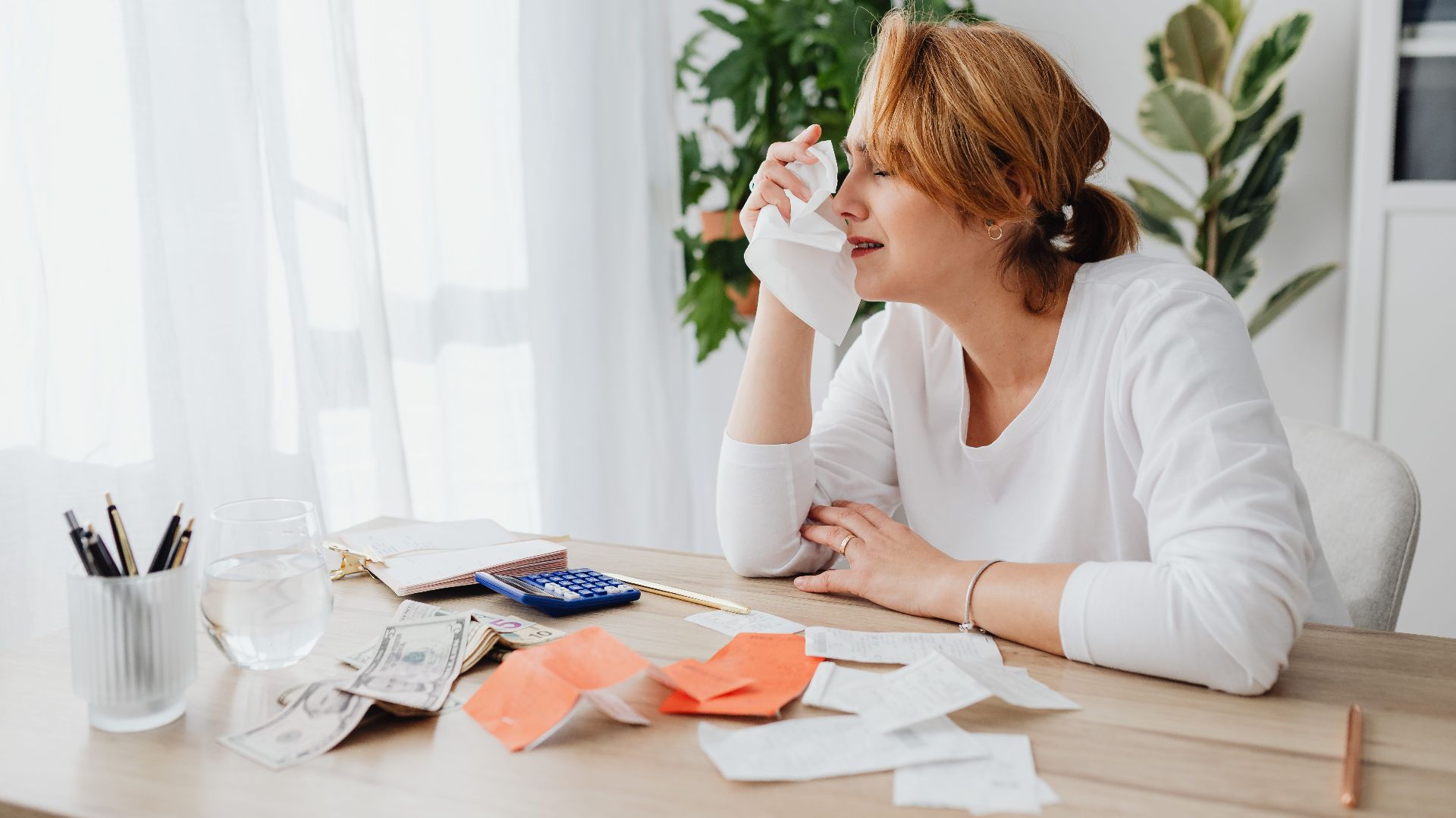 A woman is overwhelmed by bills and finances, sitting at a desk indoors.