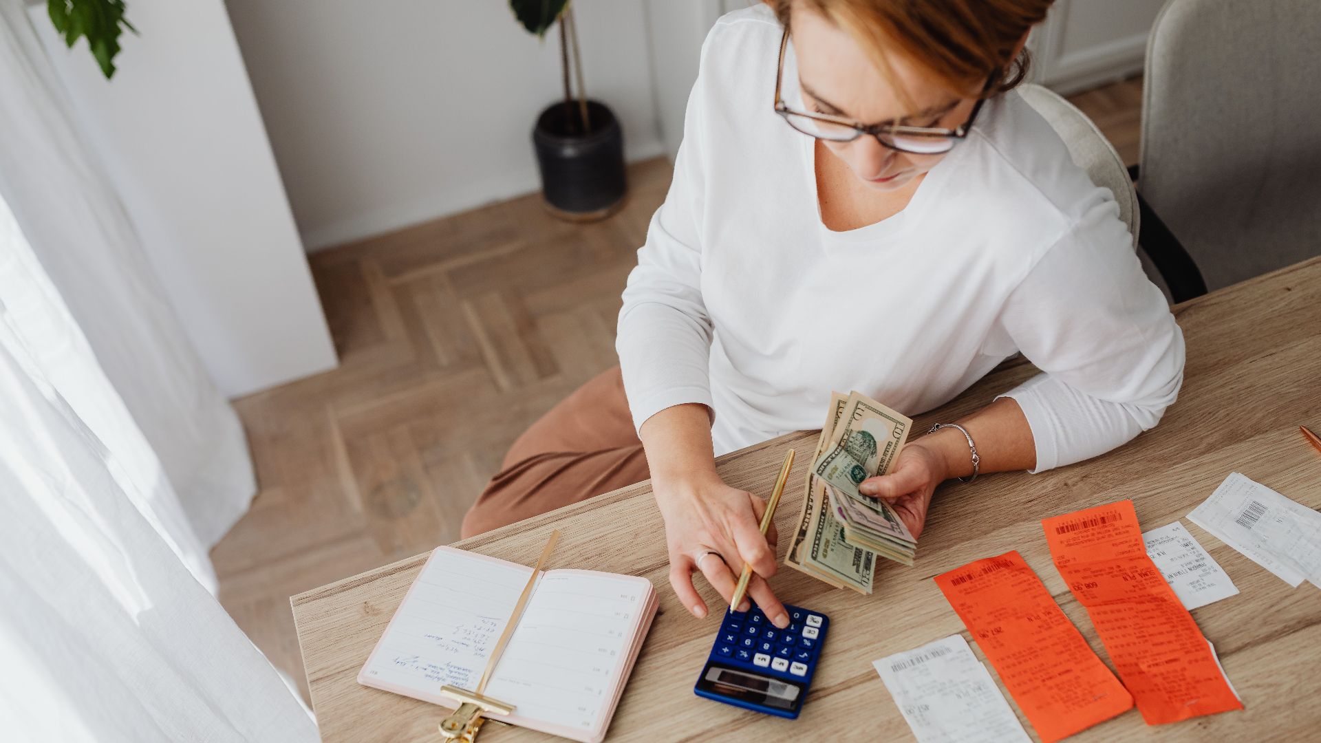 Top view of a woman managing finances with a calculator, cash, and bills in a home setting.