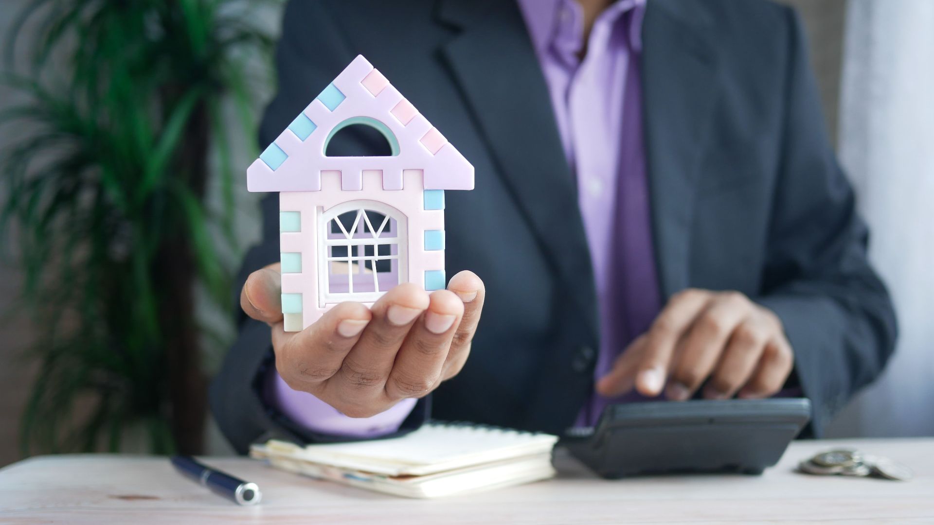 Businessman in suit holds model house, calculates real estate investments.