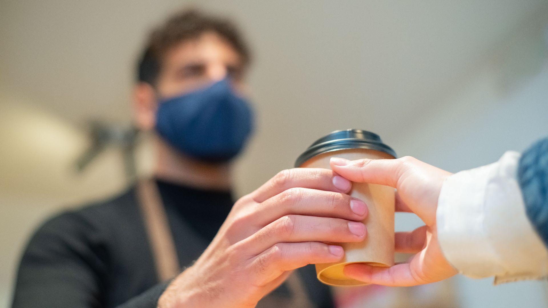 Barista hands over a to-go coffee cup with a focus on hand hygiene and service.