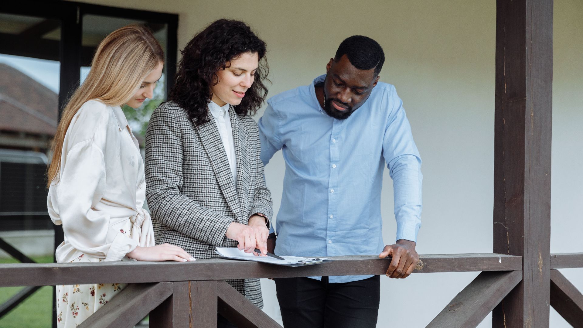 Real estate agent discussing property paperwork with a couple on a porch.