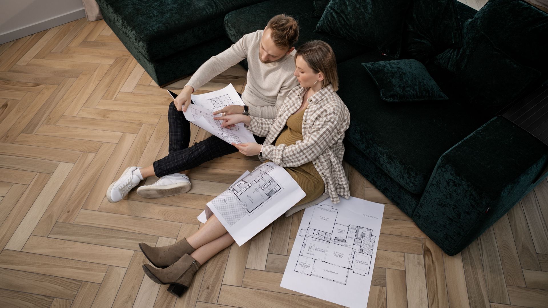 A couple sits on the floor reviewing architectural blueprints, planning their new home.