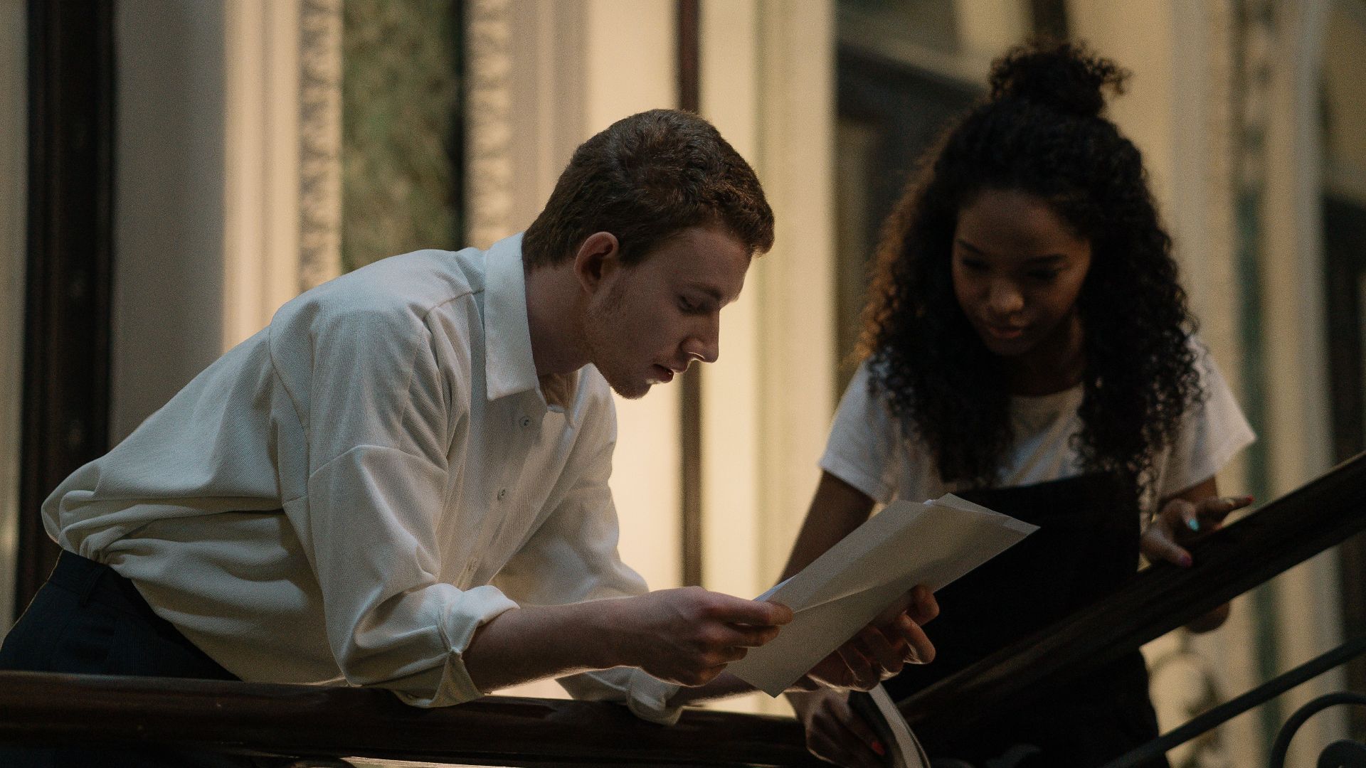 Two young students leaning over handrails, examining study materials inside a stylish building.