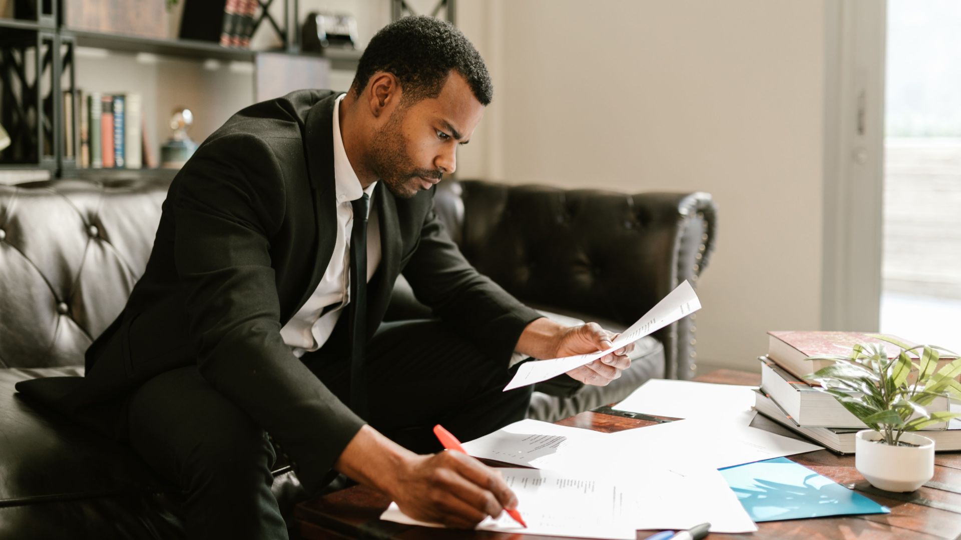 Man in suit signs papers at a coffee table indoors, symbolizing professionalism.