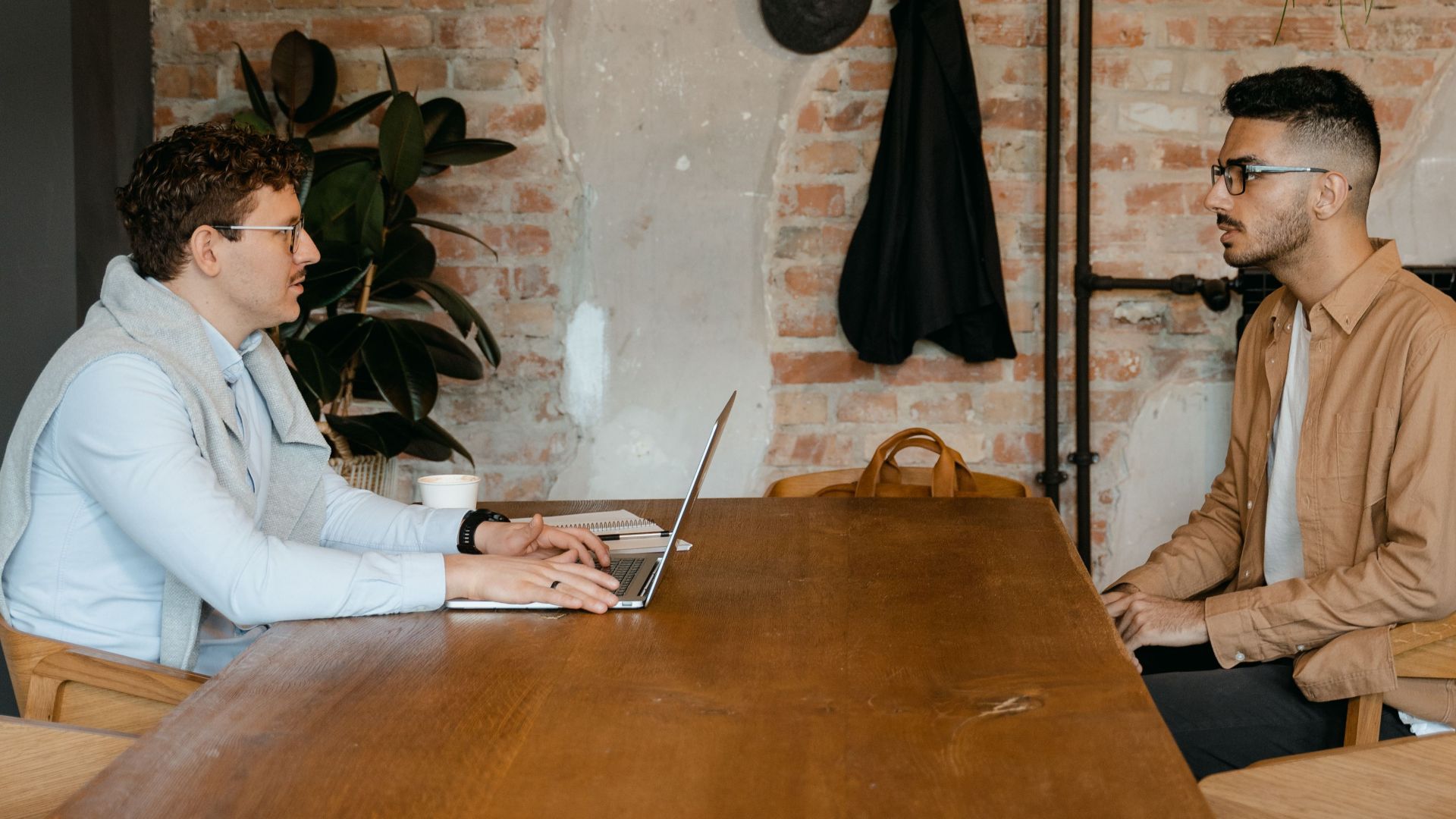 Two men in a modern office having a business discussion across a wooden table.