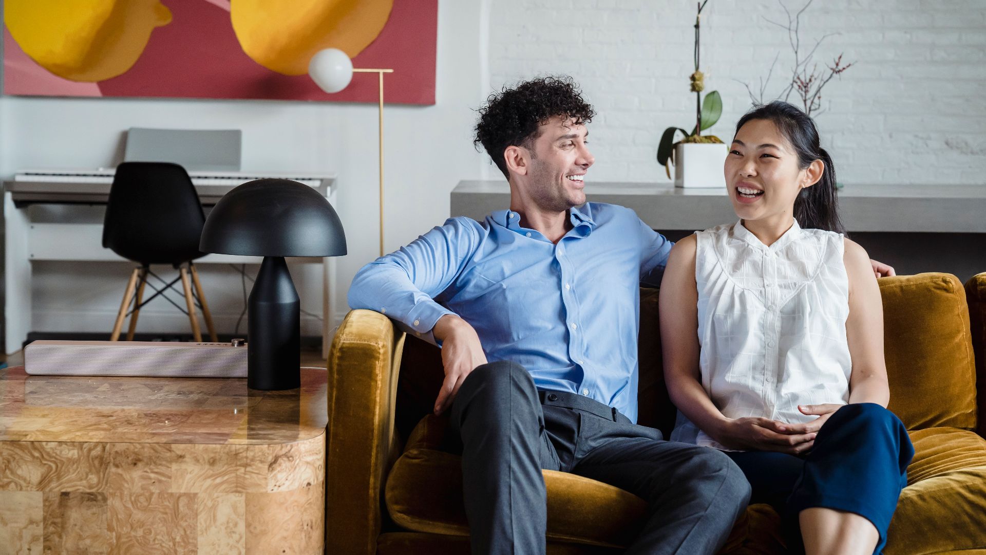 Asian woman and caucasian man laughing on a couch in a stylish living room setting.