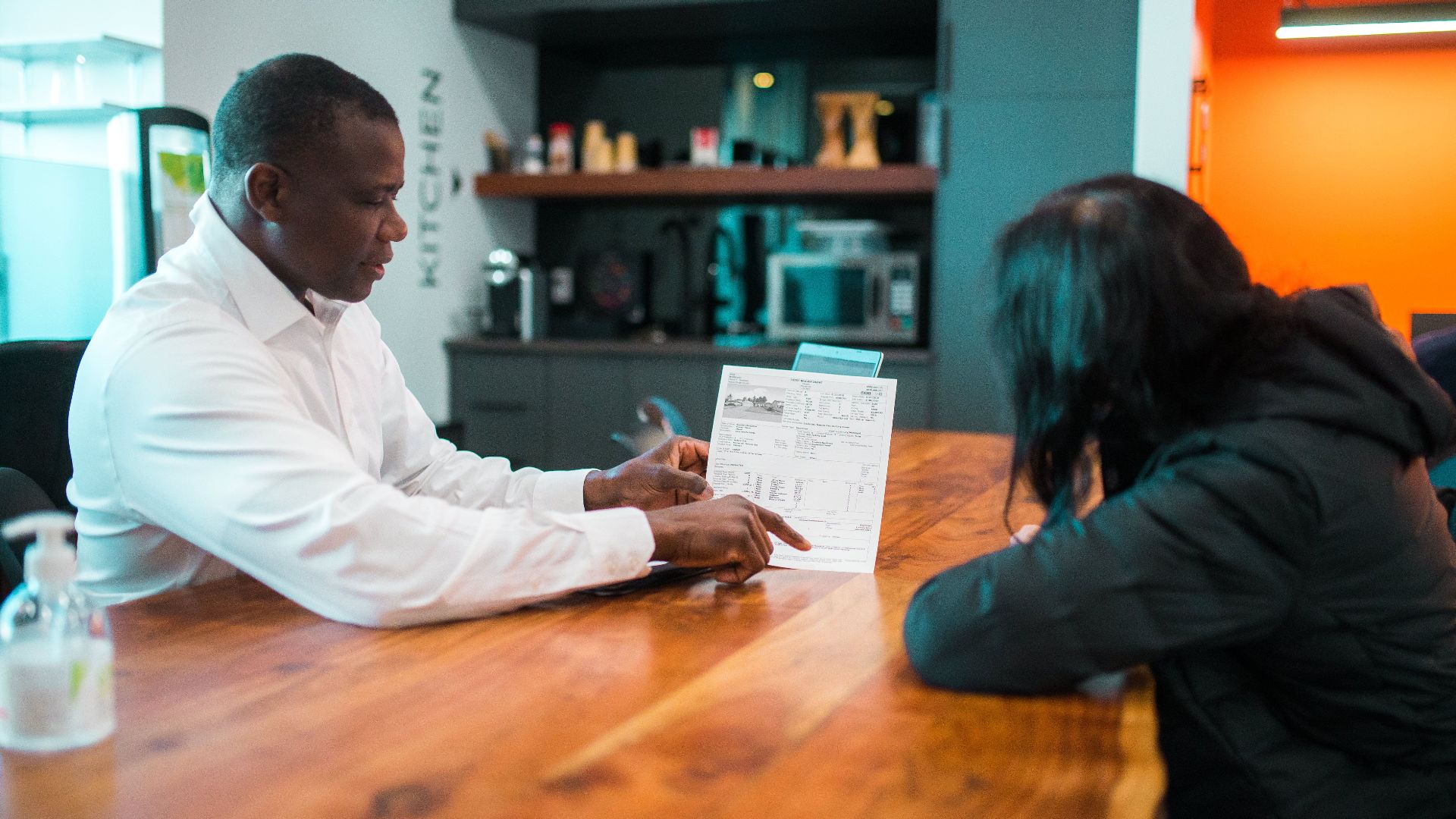 Business meeting between colleagues discussing a document indoors at a wooden table.