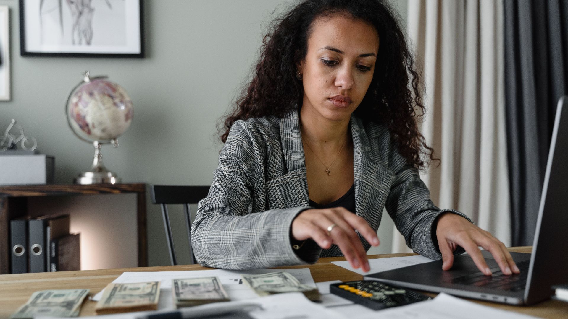 Professional woman analyzing financial documents and counting cash at office desk.