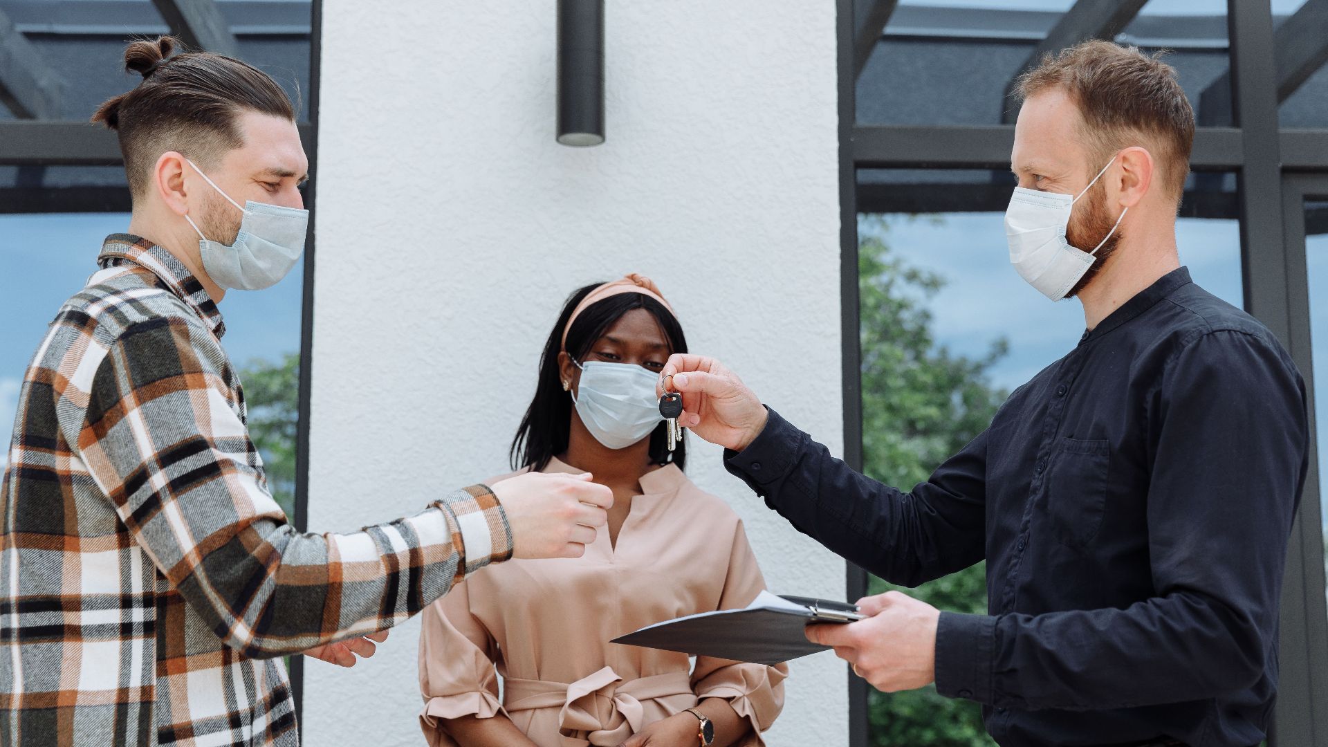 Real estate agent handover keys to a diverse couple wearing face masks, outdoors.