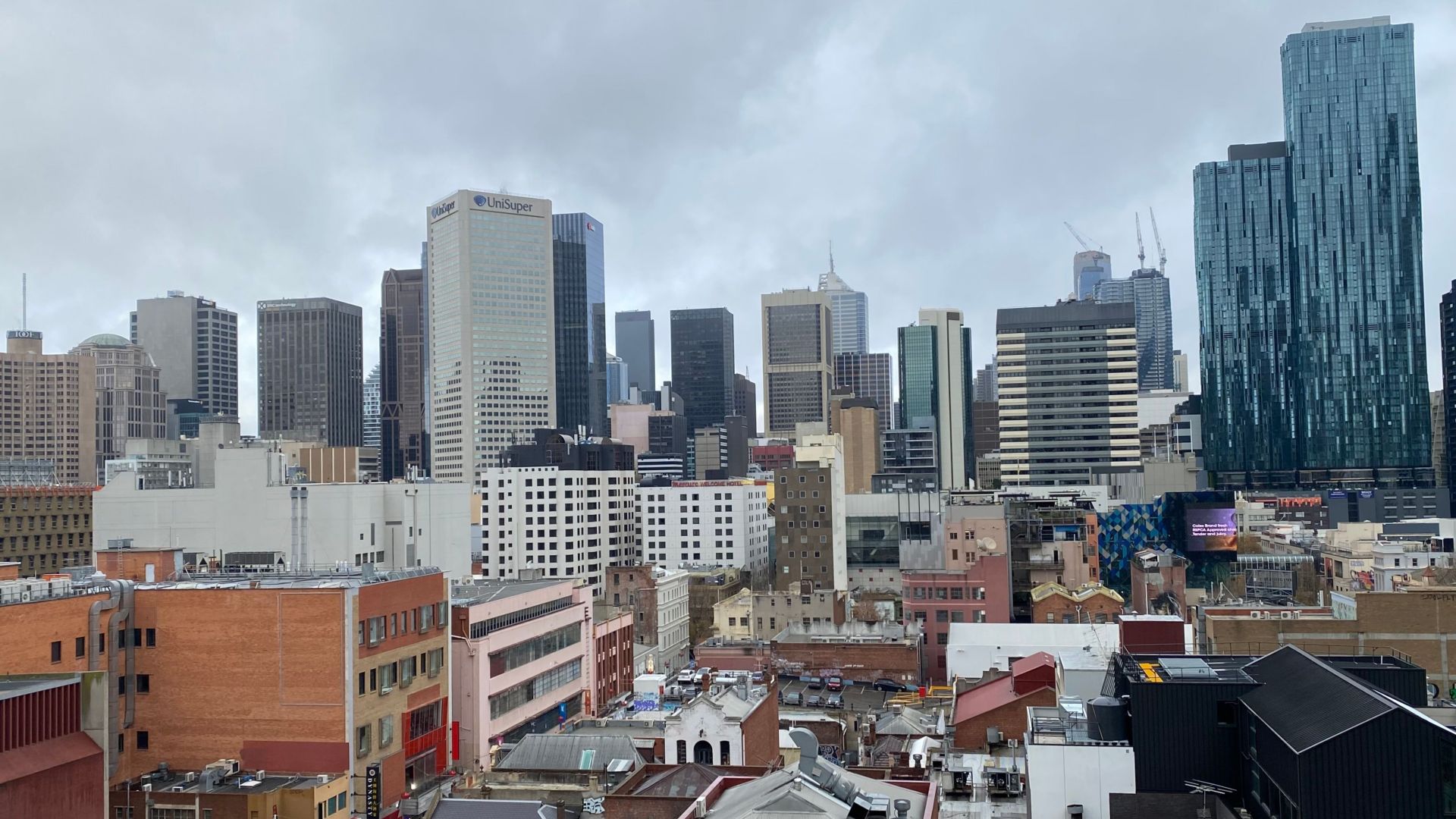 Aerial view of Melbourne's skyline under cloudy skies, showcasing modern architecture and urban life.