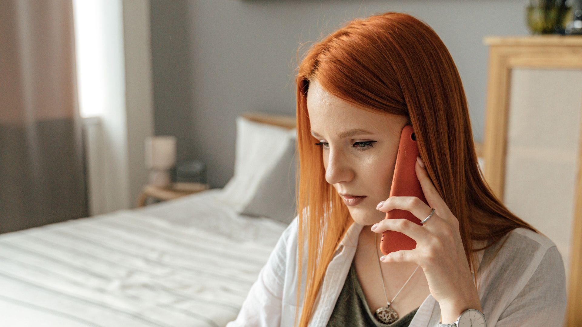 Redhead woman sits at a desk, focused on floor plans, using a smartphone, and working from home.