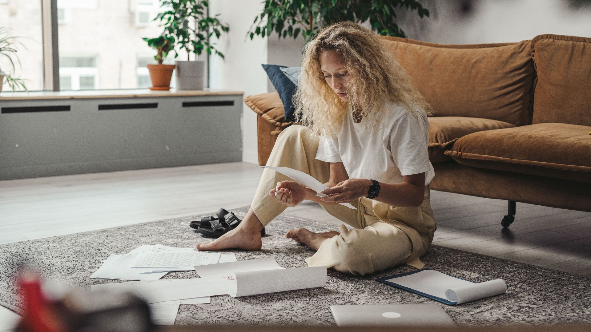Woman sitting on the floor at home, reviewing paperwork in a relaxed environment.