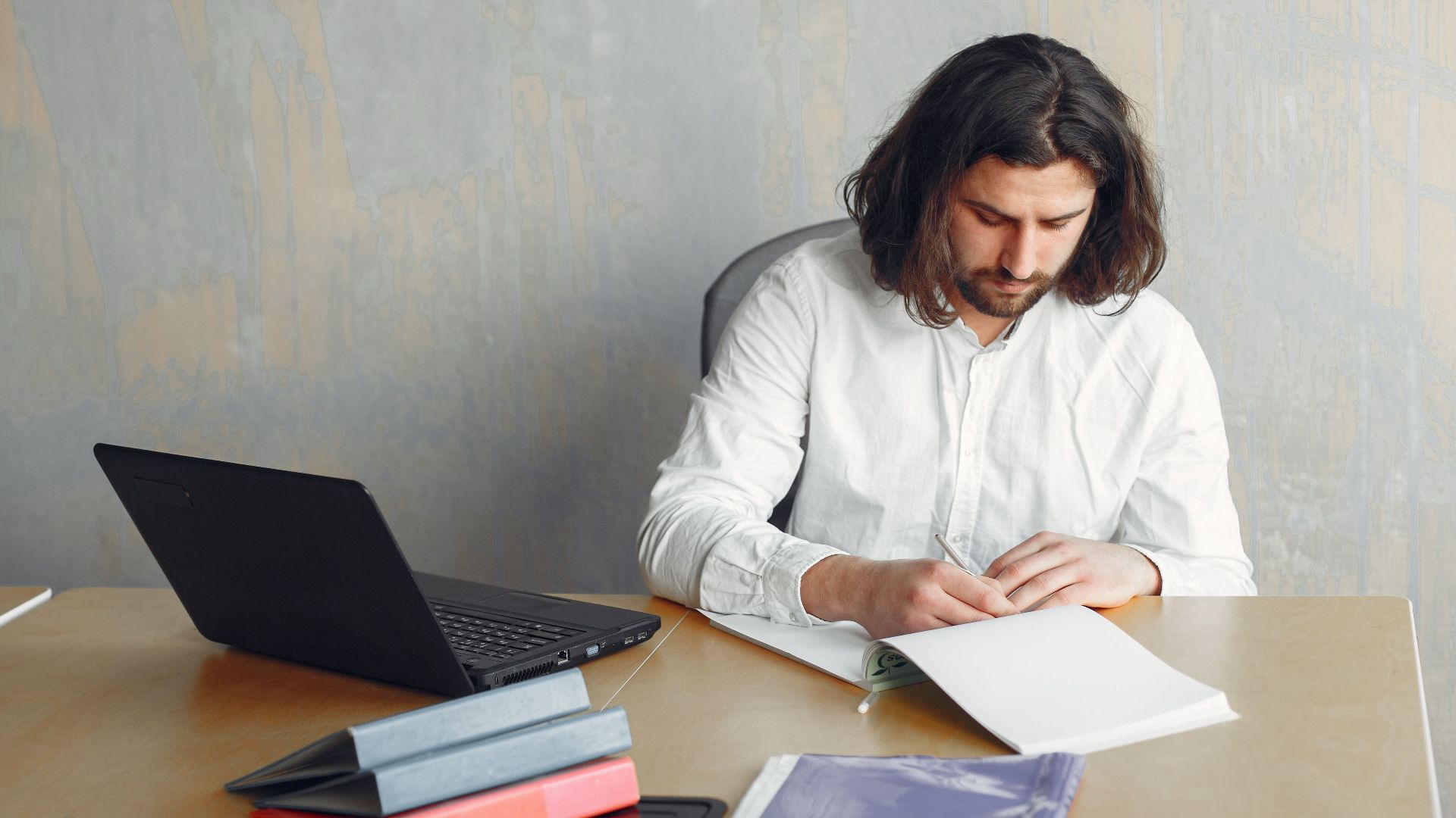 Bearded man working remotely at a minimalist desk with modern technology and paperwork.