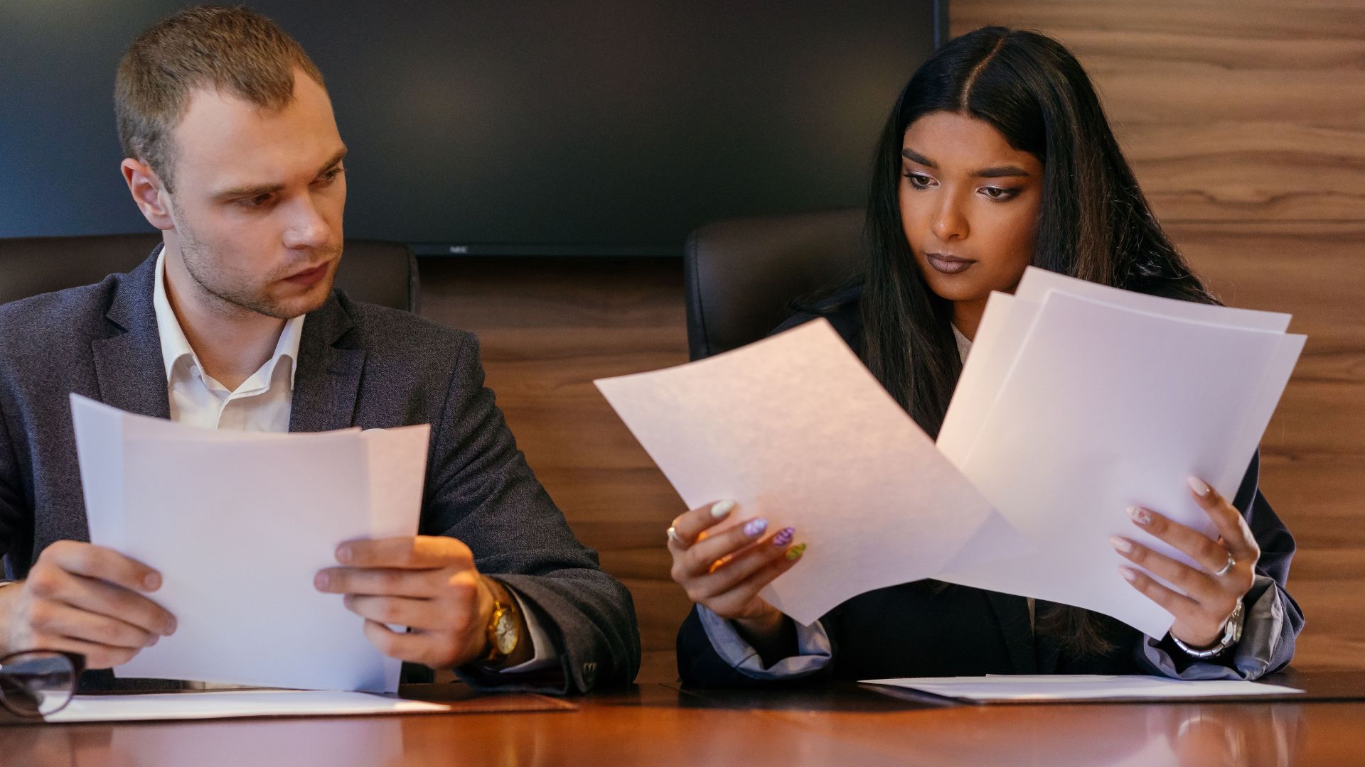 Two diverse professionals reviewing documents in a modern office setting, showcasing teamwork and focus.