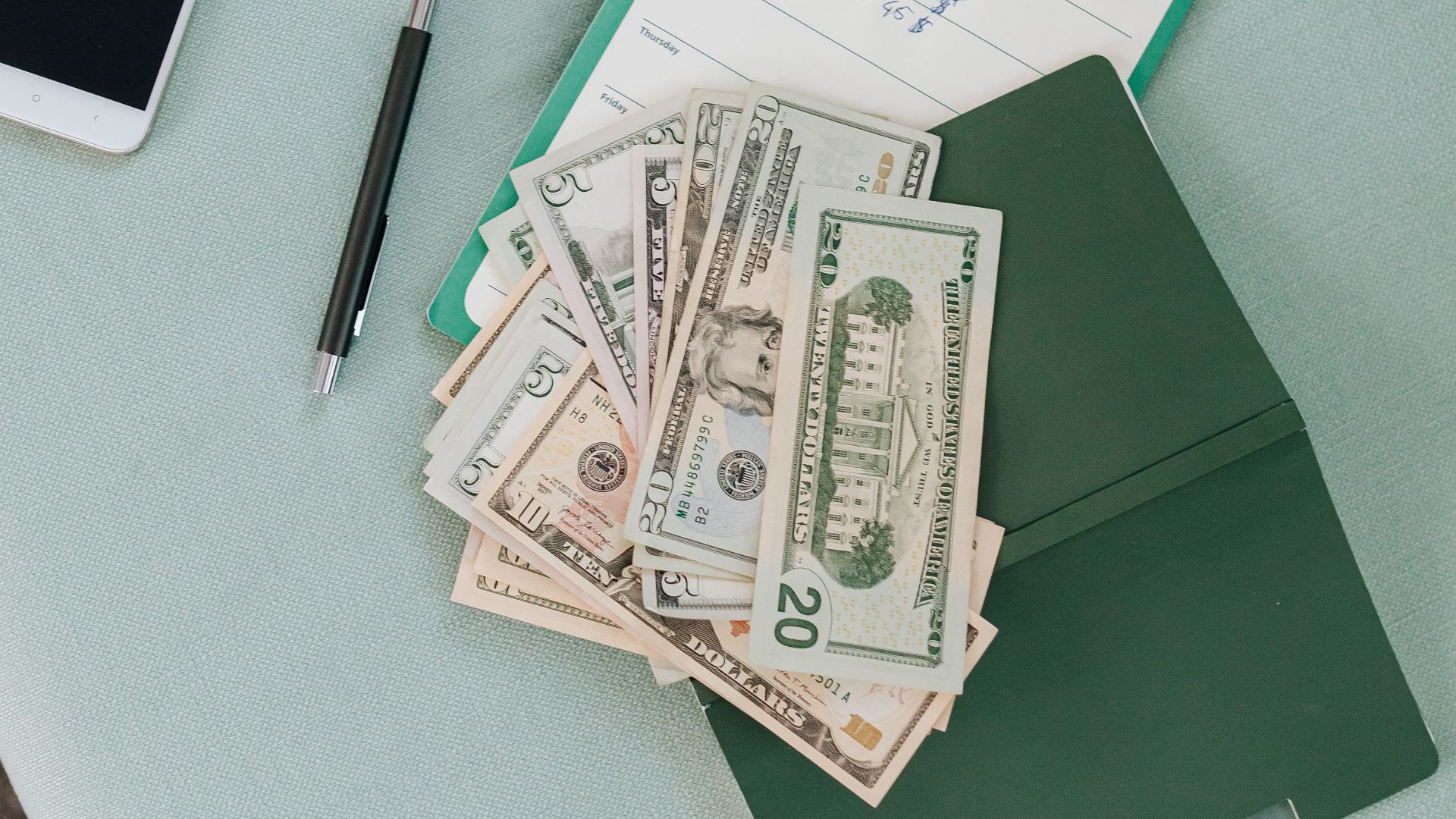 Flat lay of money, phone, and notebook on a mint sofa. Perfect for finance and budgeting themes.