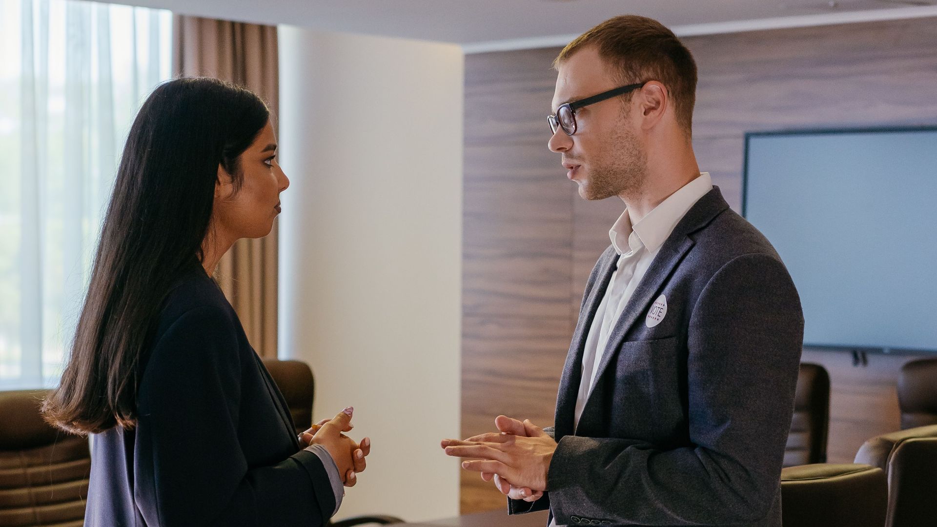 Two professionals engaged in discussion inside a modern conference room setting.