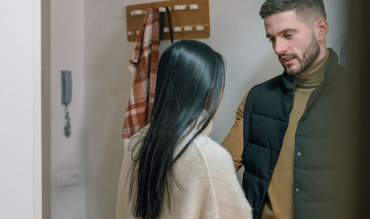 A man and woman talk inside a cozy home. They appear engaged in a conversation