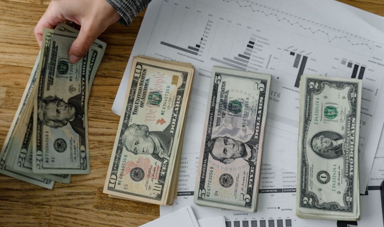 Person holds US dollars over financial papers, showing income or budget analysis
