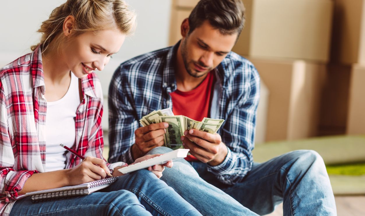 young couple counting money while sitting on floor in new apartment
