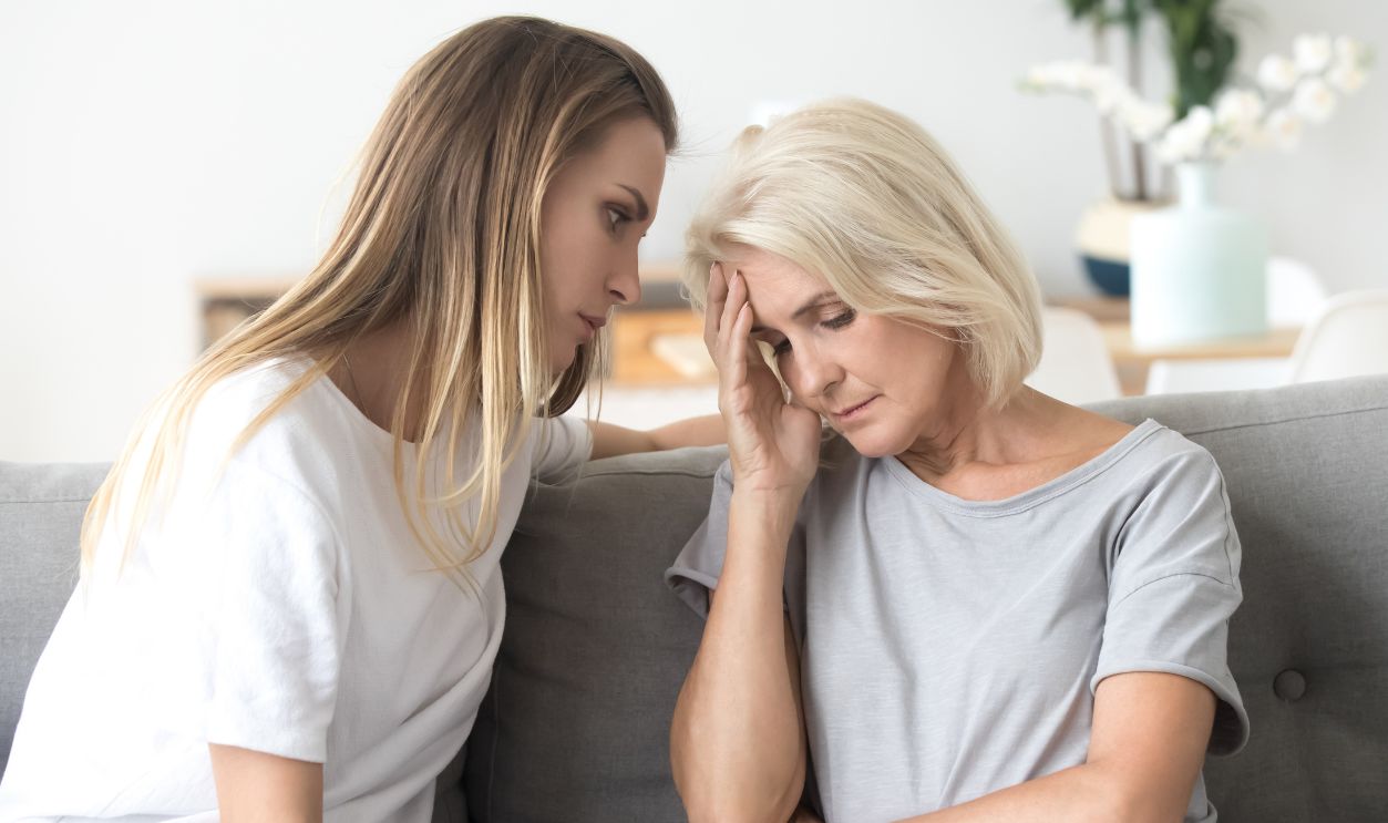 Loving daughter comforting, consoling aged upset mother, worrying for her health, sitting together on sofa at home, mature woman having problem, receive bad news, suffering from headache