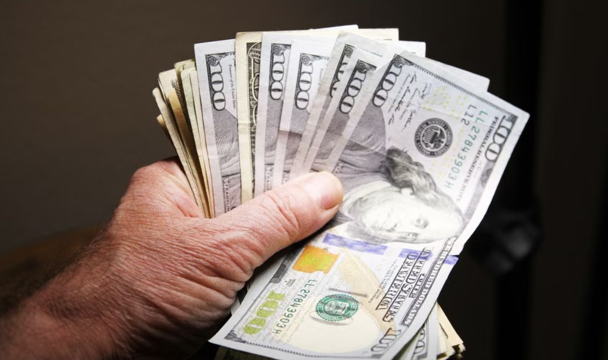 Close-up of a hand holding multiple hundred dollar bills on a dark background