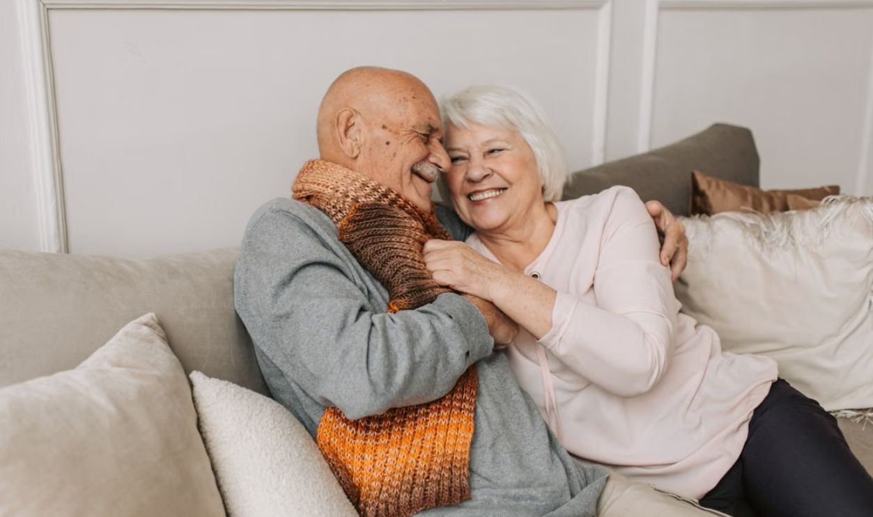 Happy elderly couple embraced in a cozy home setting, sharing joyful smiles.
