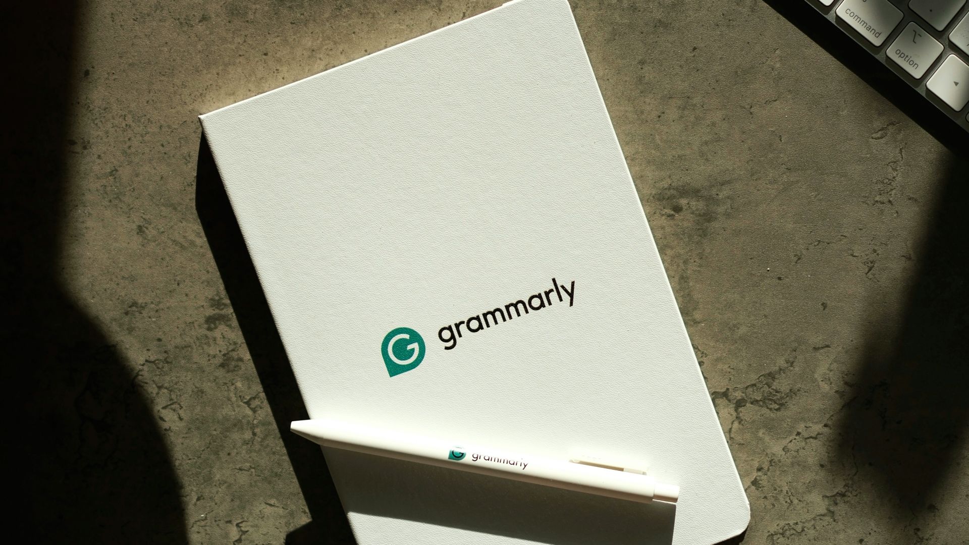 Grammarly notebook, pen, and keyboard on a desk.