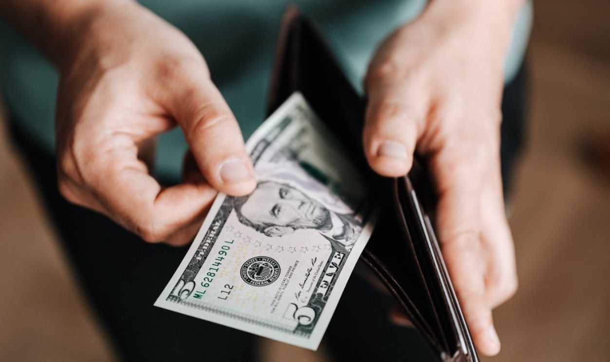 A person taking a five dollar bill from a wallet symbolizing personal finance and budget management