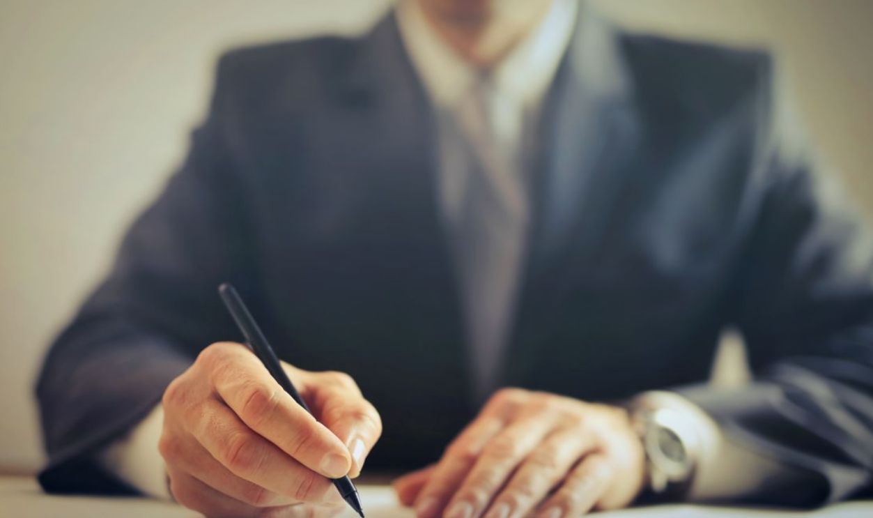 Faceless businessman in suit signing a contract at office desk, focused on task