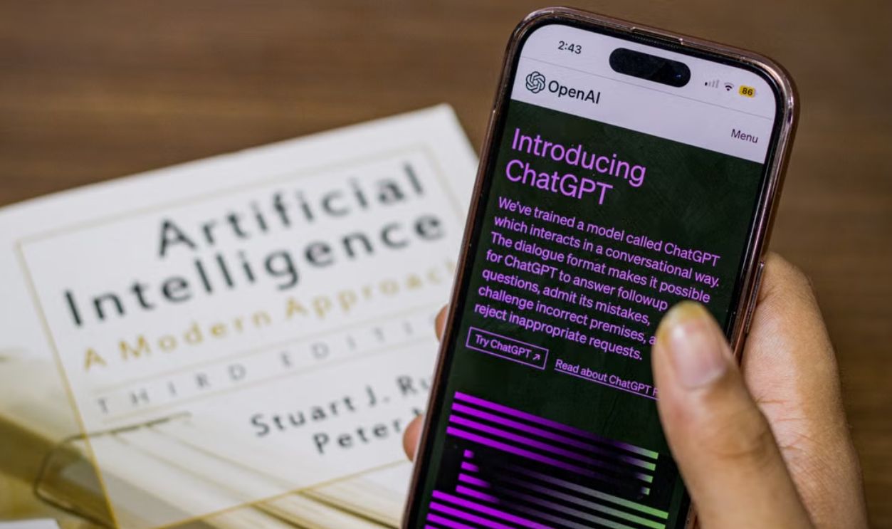 Close-up of a smartphone displaying ChatGPT app held over AI textbook